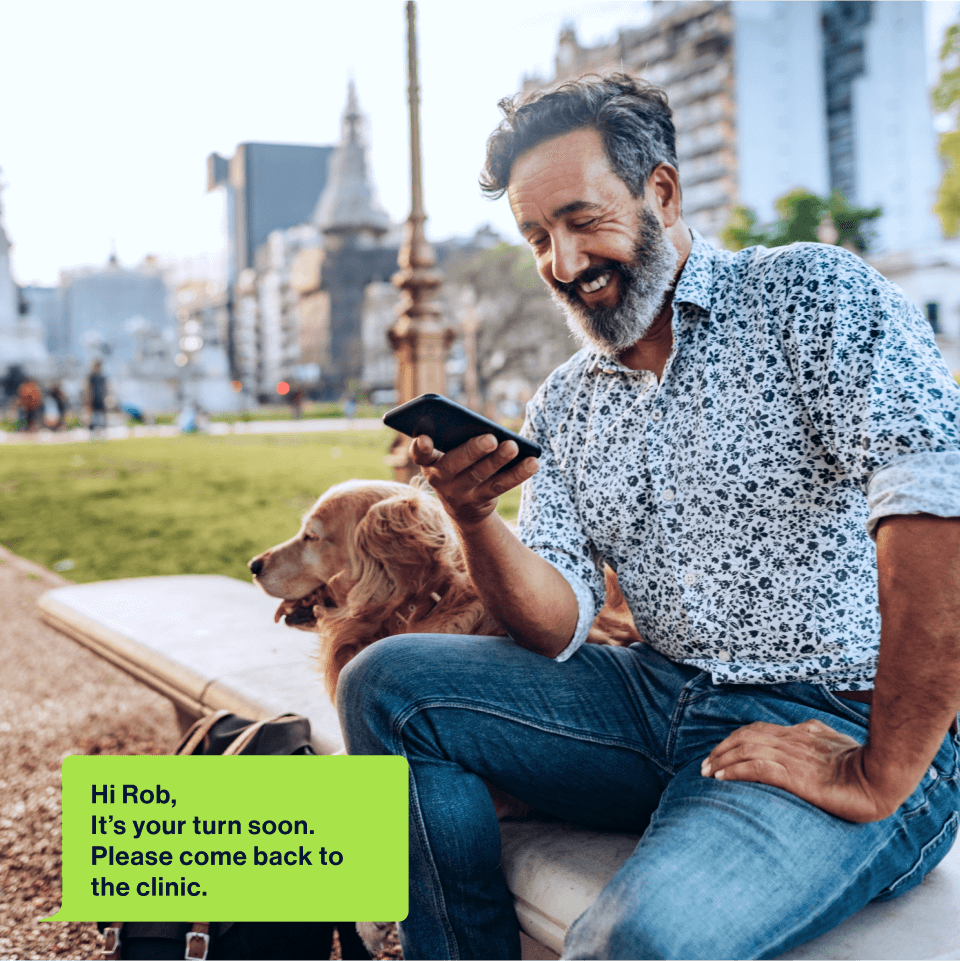 Man in park with dog receiving SMS for queue line