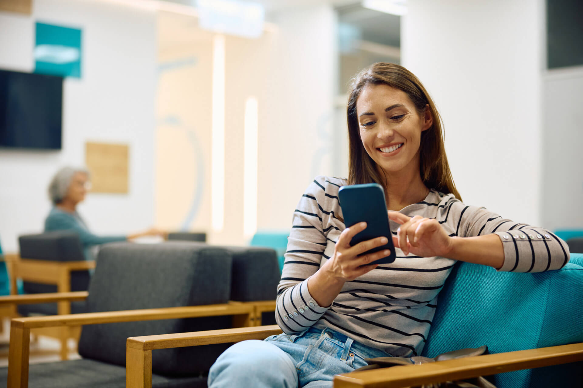 Young happy woman using cell phone in waiting room at doctor